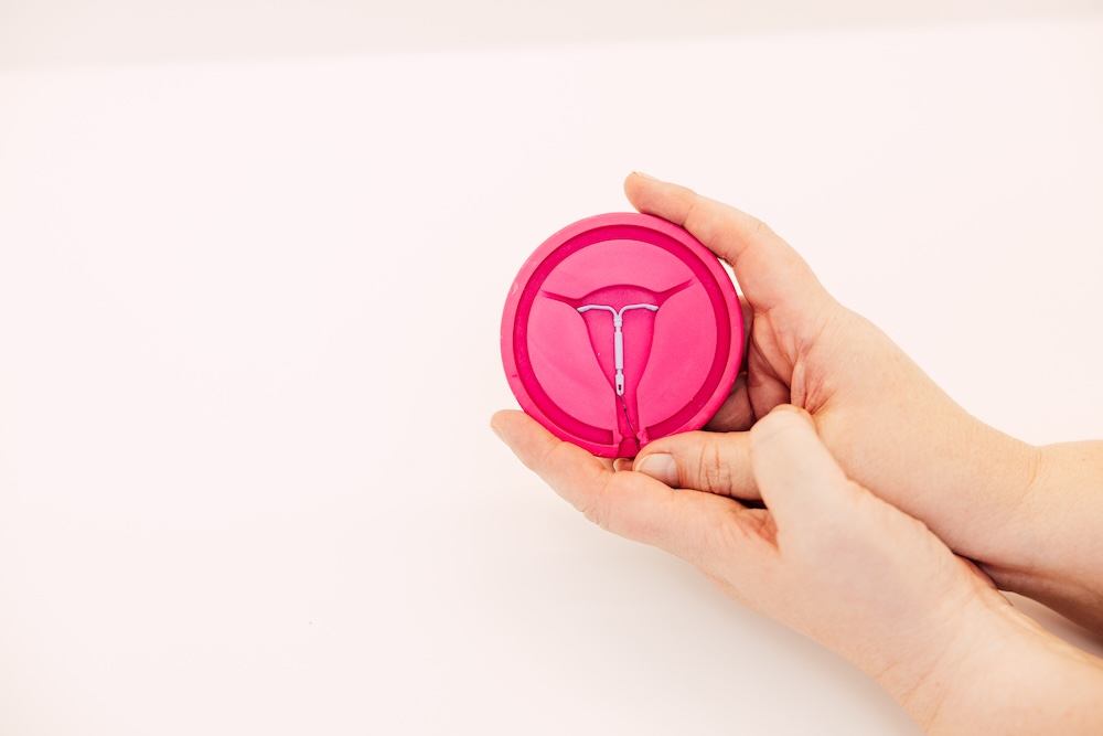 Hände halten eine pinke Box mit Spiralen-Symbol zur Verhütung